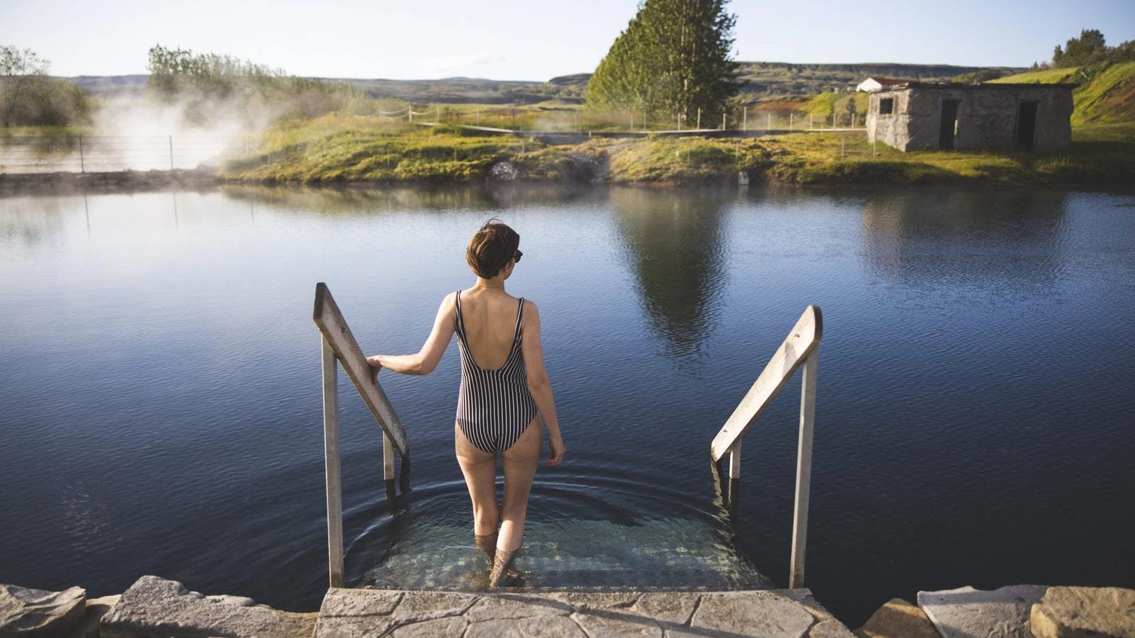 Woman in striped swimsuit walking into the secret lagoon on a golden circle day tour during summer