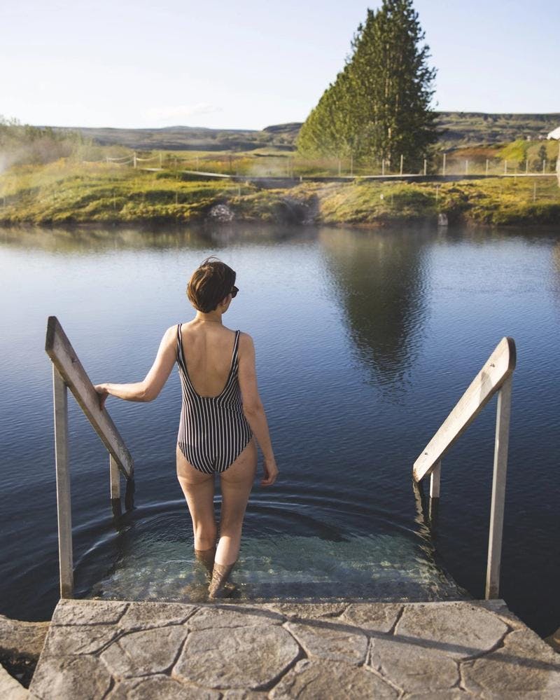 Woman in striped swimsuit walking into the secret lagoon on a golden circle day tour during summer