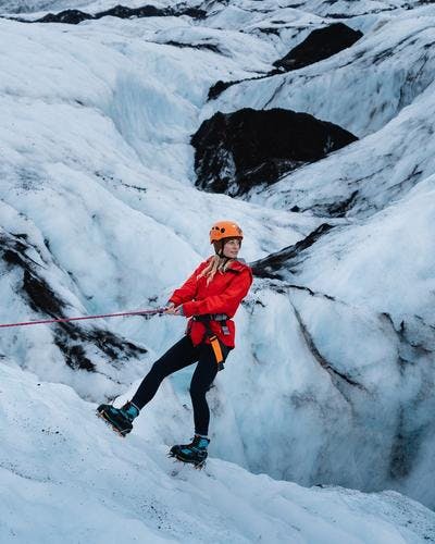 woman on a glacier hiking tour in red jacket and orange helmet descending on ice