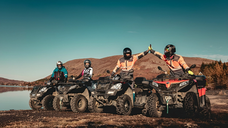Four people on a ATV tour in Icelandic nature, blue sky, mountains and a lake in background.