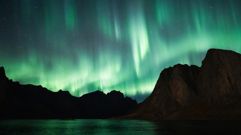 The aurora borealis gracefully dancing across the sky above mountains.