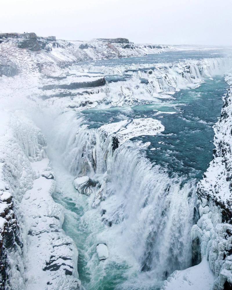 Gullfoss waterfall covered in Ice on a cold winter day. Tourists on a Golden Circle tour can be seen in the distance.