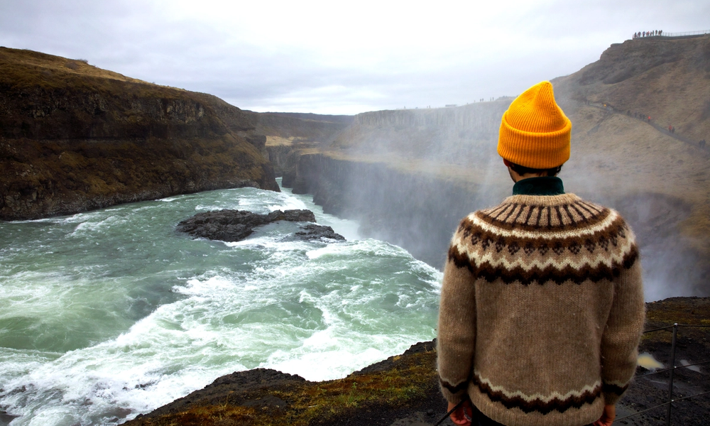 a traveller in yellow hat and icelandic sweater staring at gullfoss on golden circle tour in iceland