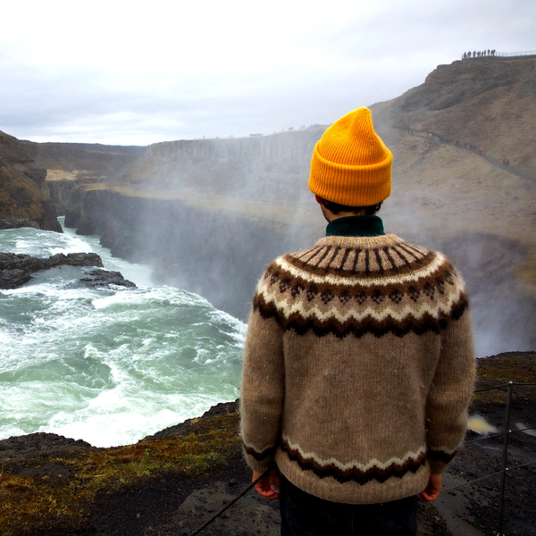 a traveller in yellow hat and icelandic sweater staring at gullfoss on golden circle tour in iceland