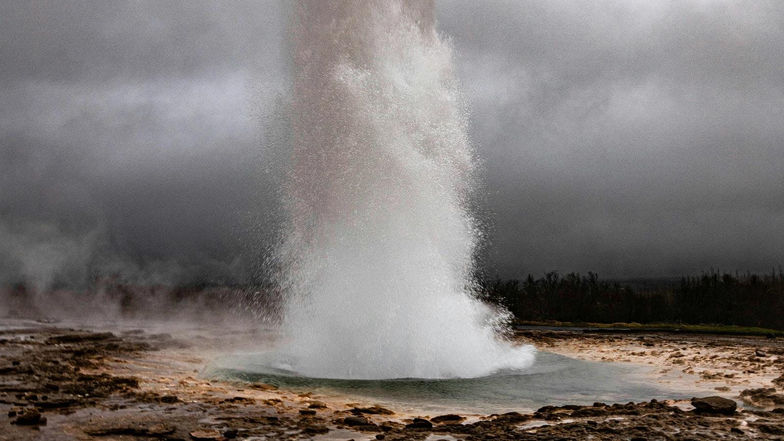 Strokkur erupting in the Geysir hot spring area on a cloudy summer day.