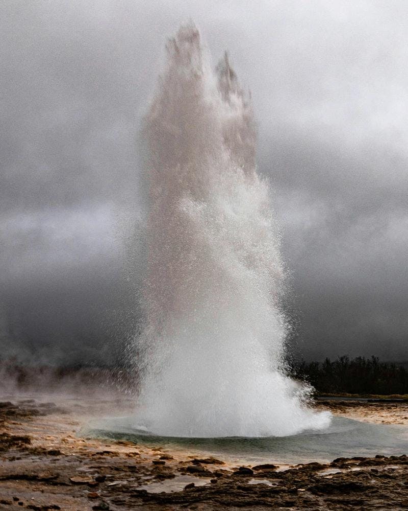 Strokkur erupting in the Geysir hot spring area on a cloudy summer day.
